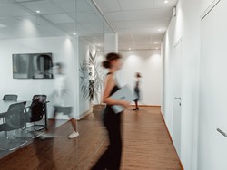 Modernes Büro mit Glasfront, bewegte Menschen sind verschwommen zu sehen.